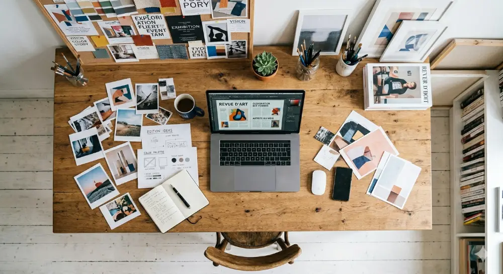 Vue plongeante d'un bureau de création : polaroids, magazines, palette de couleurs et carnet